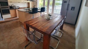 A modern kitchen with a wooden dining table, two chairs, a built-in oven, and a refrigerator. - Executive Lakeside 4 Bed Townhouse (Milton Keynes)