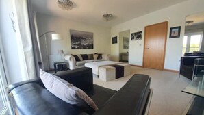 A modern living room with a black sofa, a white sofa, and a large window. - Executive Lakeside 4 Bed Townhouse (Milton Keynes)