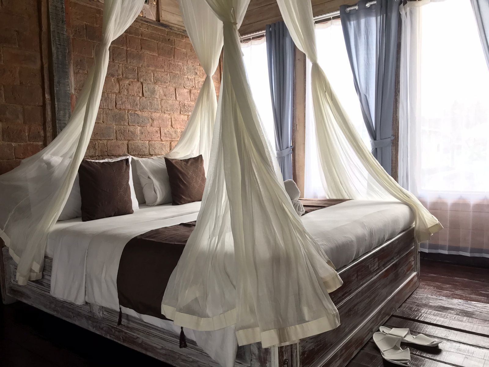 Una cama con estructura de madera, ropa de cama blanca y dosel.