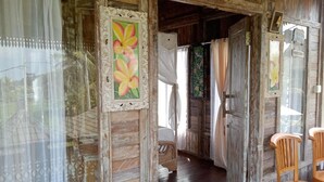 A rustic wooden room with a bed, a wooden chair, and a door leading to another room. - Ananda JJ Ubud Resort & Spa (Ubud)