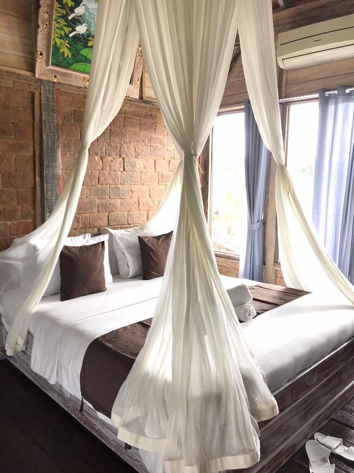 A bed with a canopy, a brick wall, and a painting on the wall.
