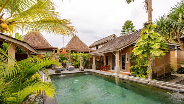 A pool surrounded by traditional buildings with thatched roofs, lush greenery, and a clear sky. - Ananda JJ Ubud Resort & Spa (Ubud)