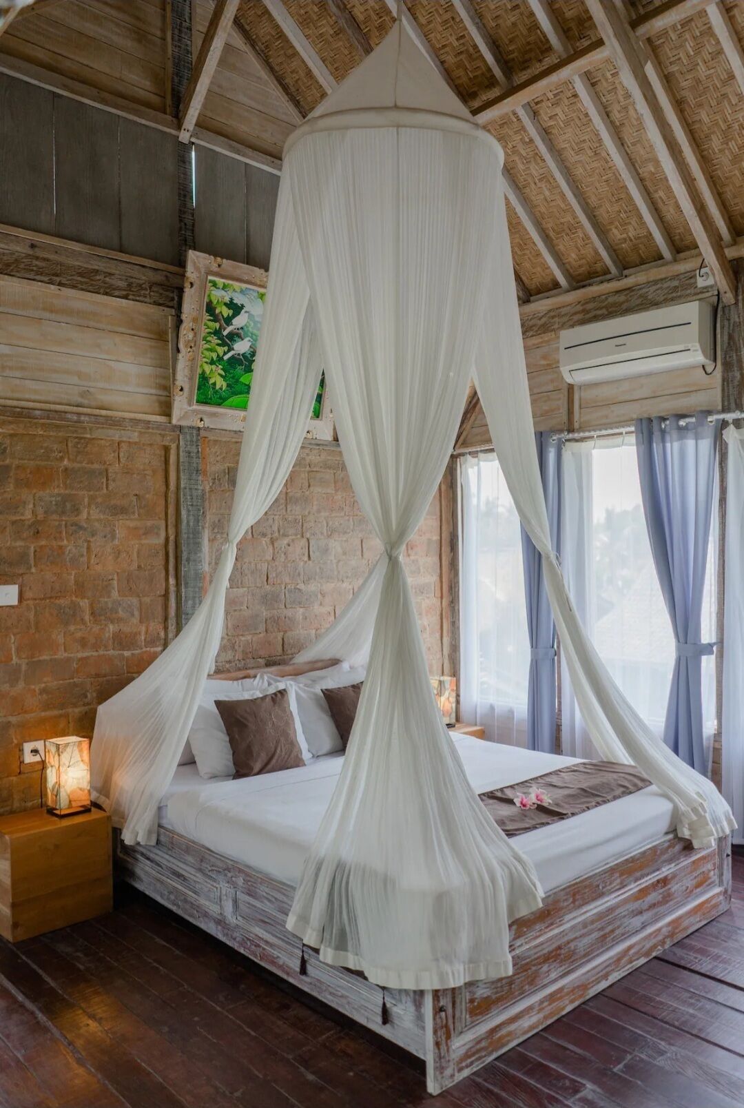 A bed with a canopy, a brick wall, a picture frame, and an air conditioning unit.