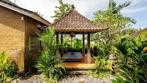 A traditional hut with a tiled roof, surrounded by lush greenery and a small garden area. - Ananda JJ Ubud Resort & Spa (Ubud)
