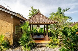 Uma cabana tradicional com telhado de telhas, rodeada por vegetação exuberante e um pequeno jardim.