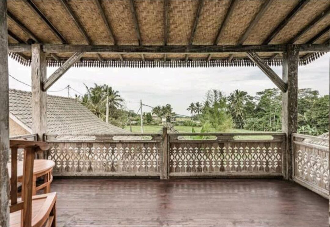A covered outdoor area with a wooden floor, a decorative fence, and a view of a residential area with houses and trees.