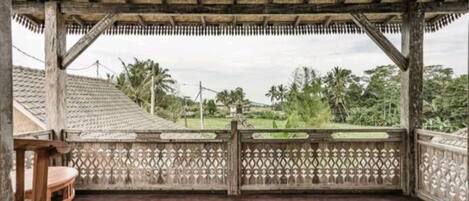 A covered outdoor area with a wooden floor, a decorative fence, and a view of a residential area with houses and trees.