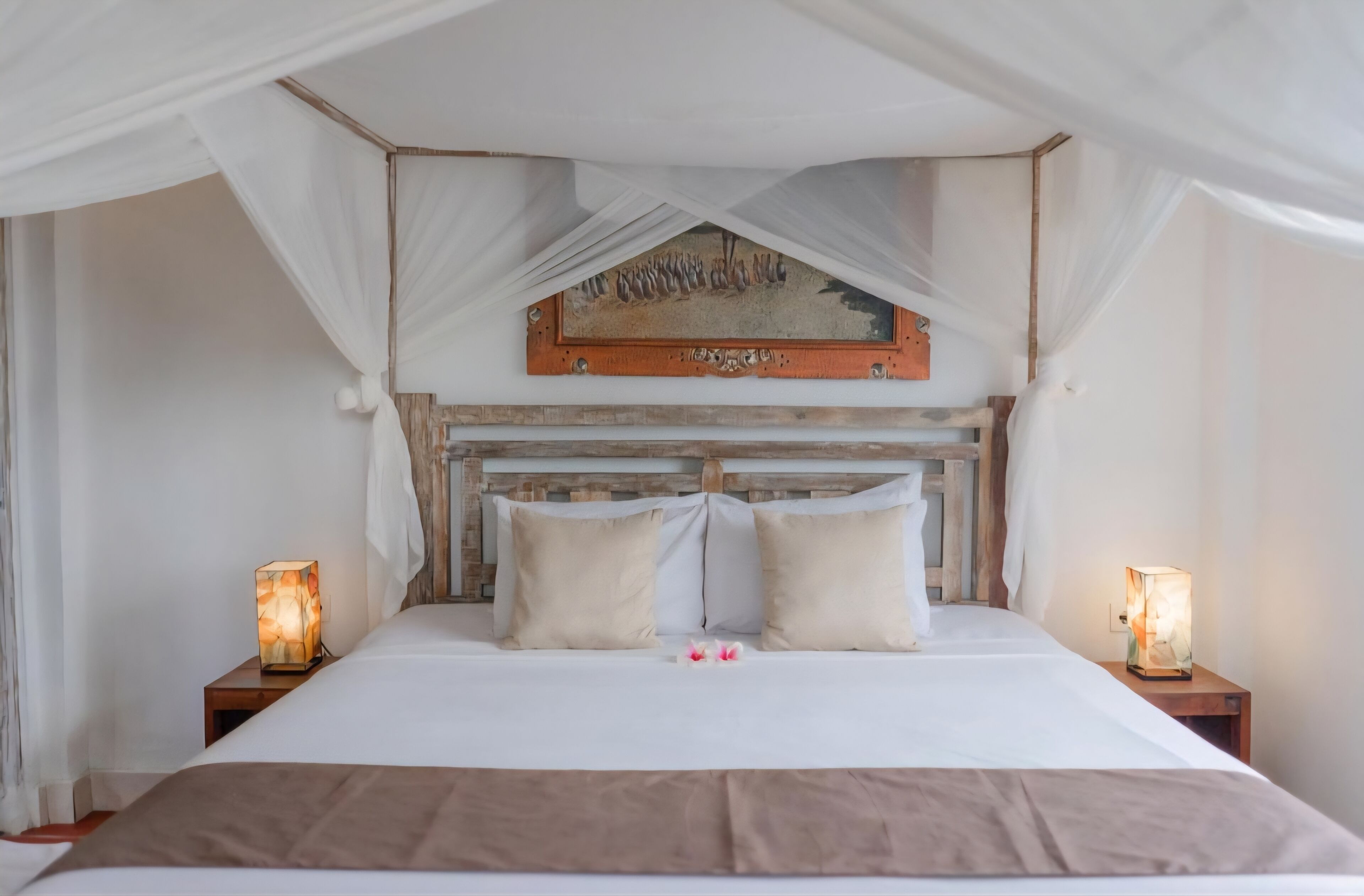 A bed with a canopy, two bedside lamps, and a framed picture above the headboard.