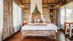 A rustic wooden room with a bed, curtains, and a window. - Ananda JJ Ubud Resort & Spa (Ubud)