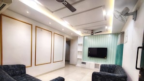 Una sala de estar moderna con dos sillones oscuros, un televisor de pantalla plana montado en una pared de acento color turquesa y ventiladores de techo.