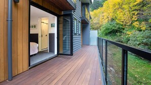 A modern building with a wooden deck and a glass door leading to a bathroom. - Private Sauna & Cold Plunge | Spacious, Close To Town | Queenstown Hill Location (Queenstown)