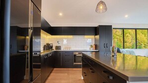 A modern kitchen with dark cabinetry, a wooden floor, and a large window offering a view of trees. - Private Sauna & Cold Plunge | Spacious, Close To Town | Queenstown Hill Location (Queenstown)