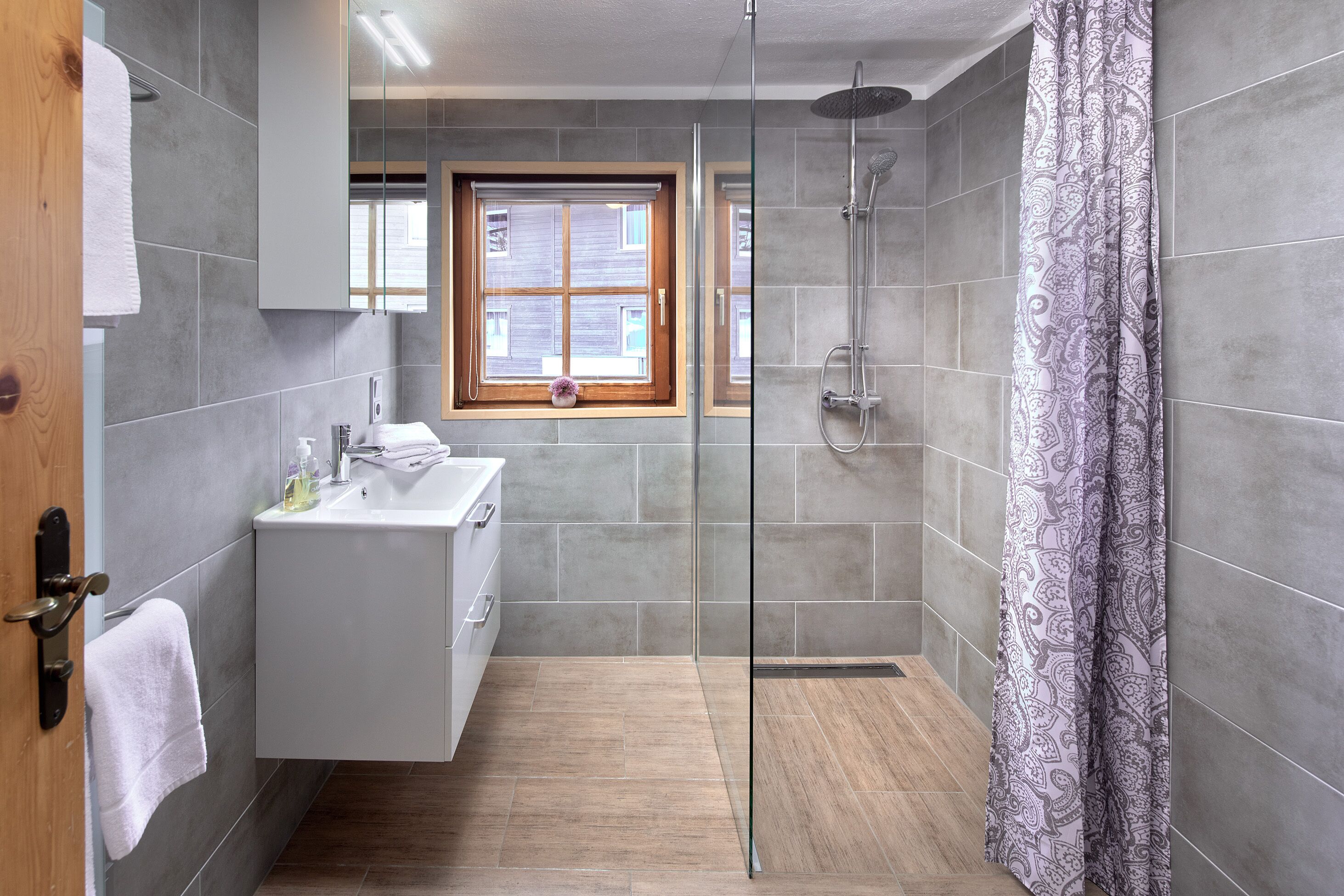 A modern bathroom with a glass-enclosed shower, a vanity with a mirror, and a window with blinds.