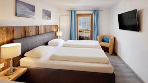 Habitación de hotel con una cama grande, cabecera de madera, televisión de pantalla plana y vistas a un balcón con cortinas azules.