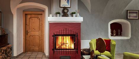 A room with a fireplace, a wooden door, a green armchair, and a tiled floor.