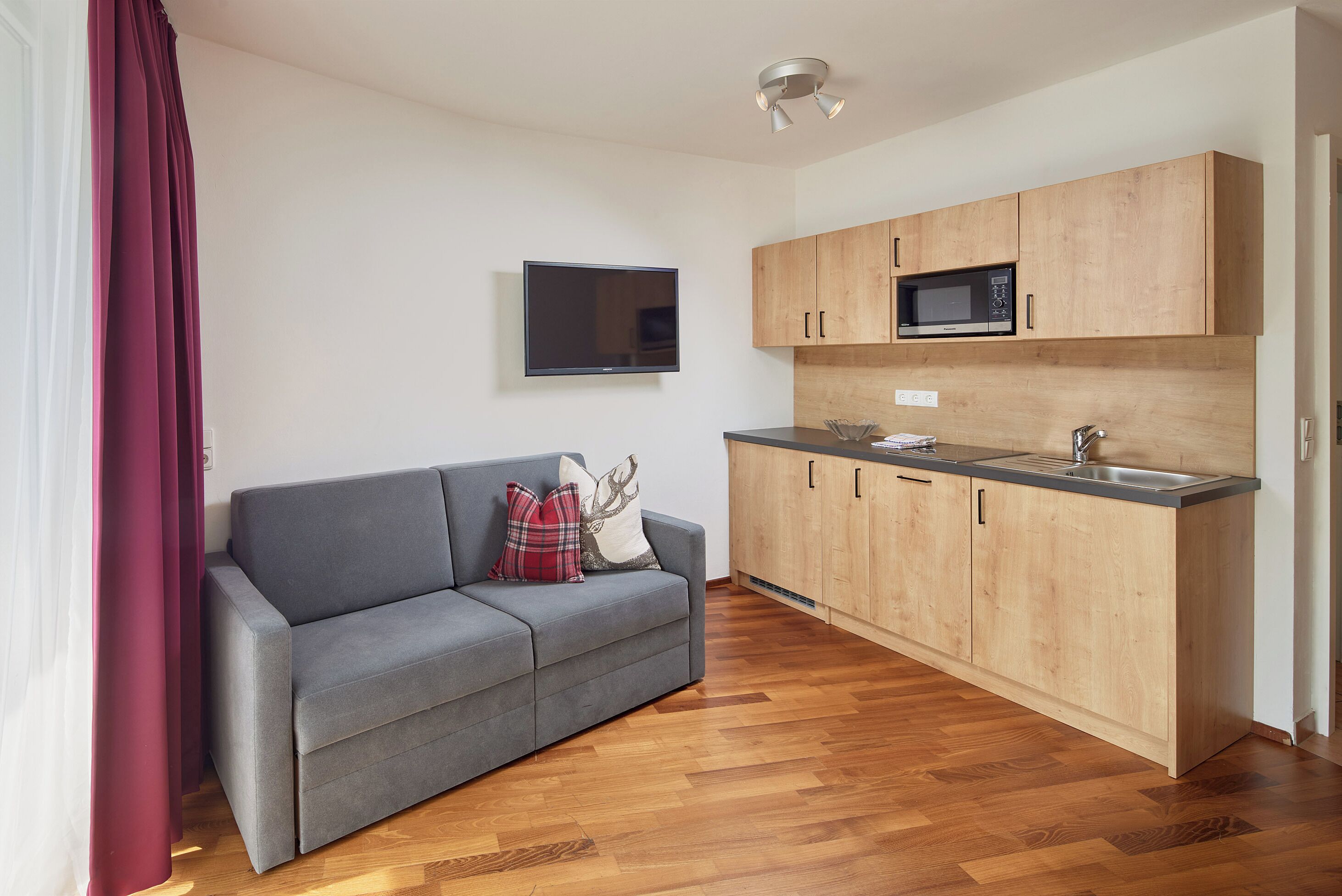 A modern kitchen with wooden cabinets, a built-in microwave, and a grey sofa with decorative pillows.