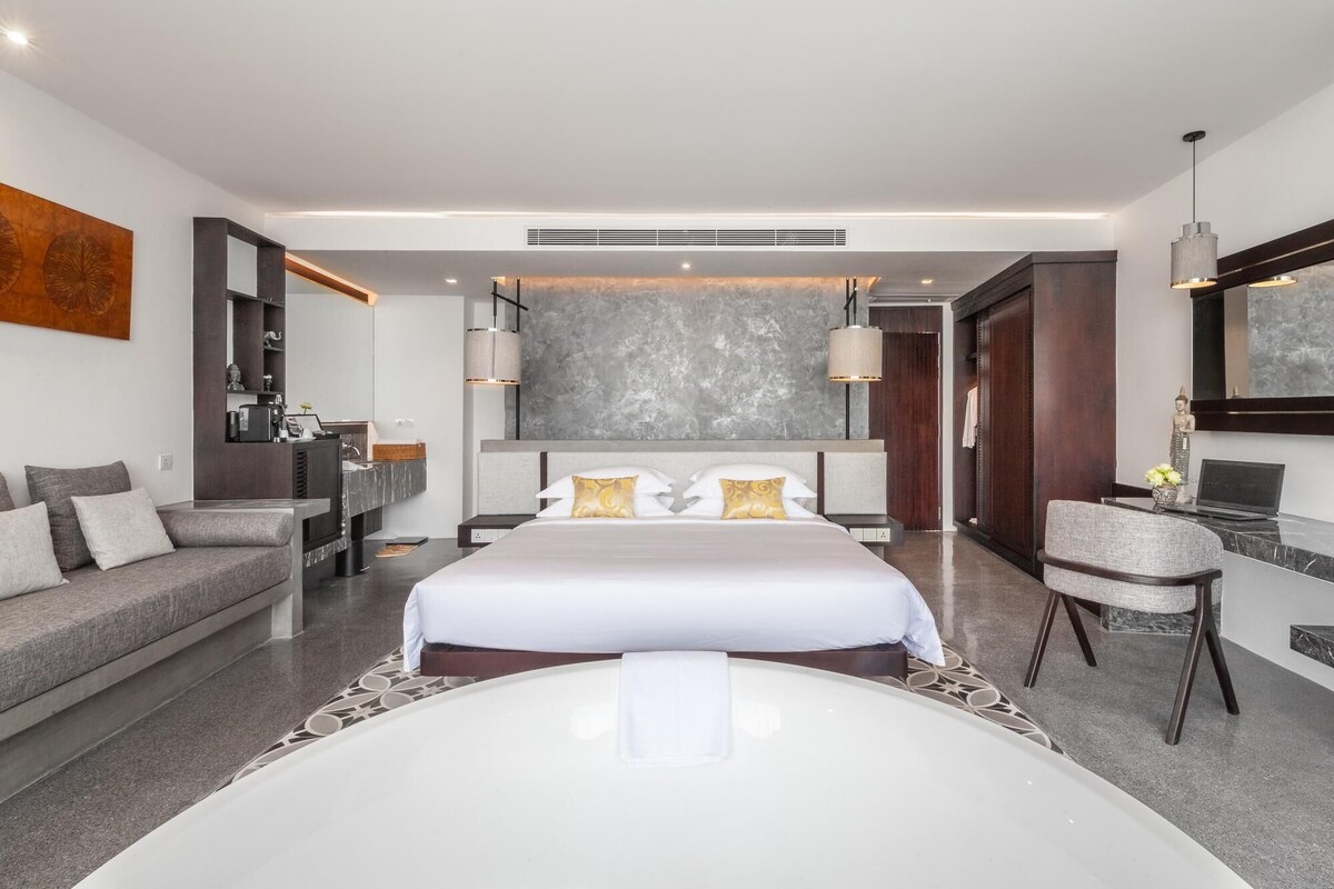 A modern hotel room with a large bed, a sofa, a desk, and a chair.