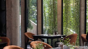 A dining area with a long table set for four, surrounded by chairs, with a view of greenery through large windows. - Hotel Vellita Siem Reap (Siem Reap)