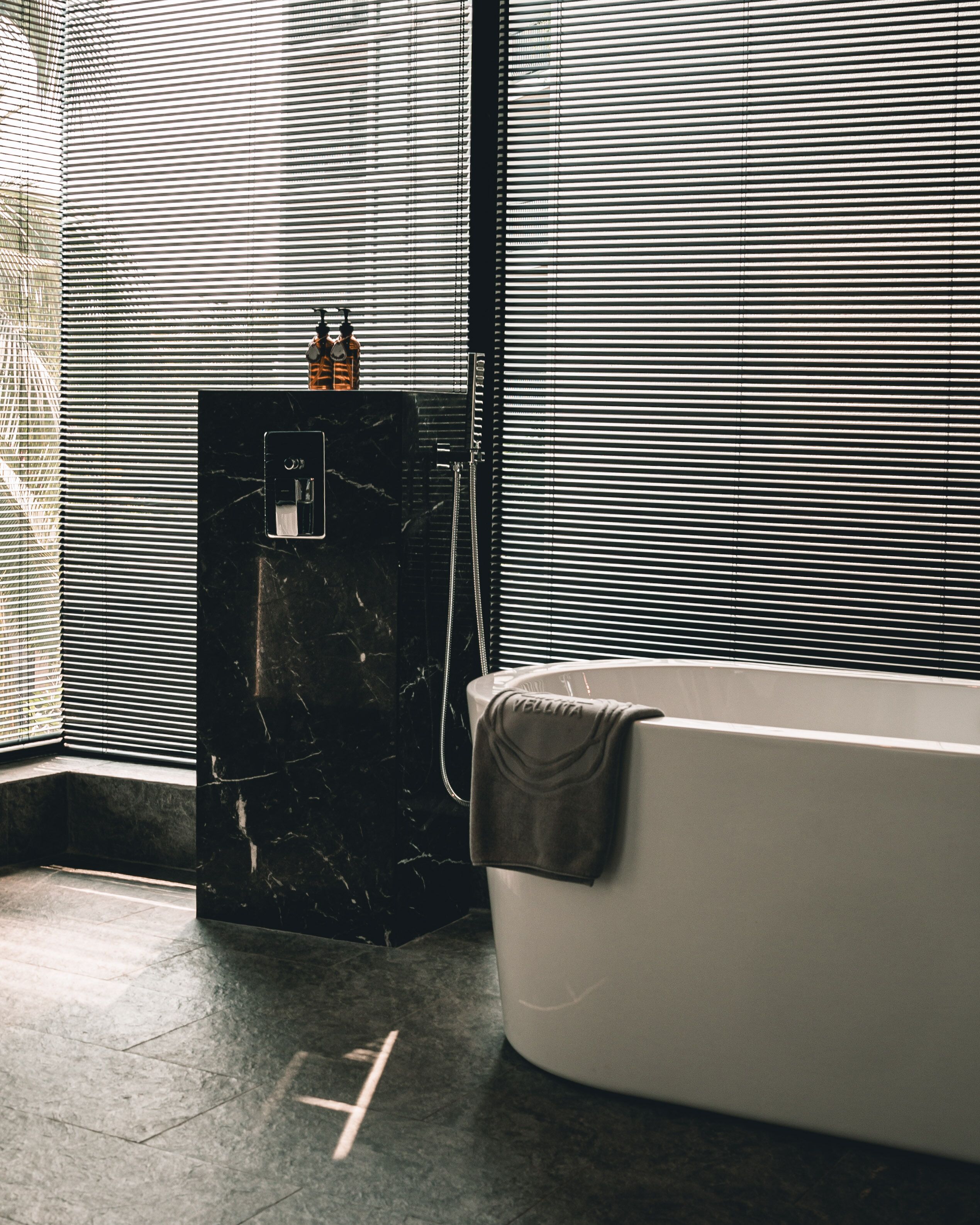 A modern bathroom with a freestanding bathtub, a marble pedestal sink, and a towel draped over the tub.
