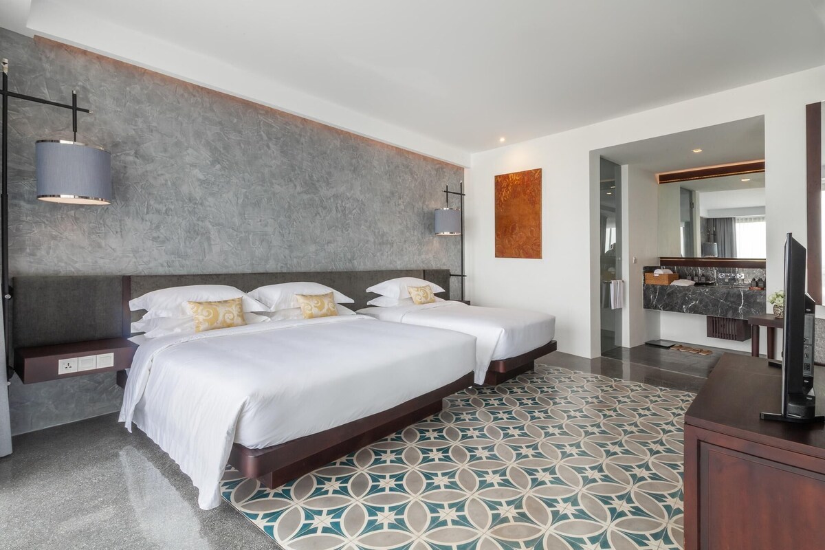 Una habitación de hotel moderna con dos camas, un cuadro abstracto grande, un baño de mármol y un televisor de pantalla plana.