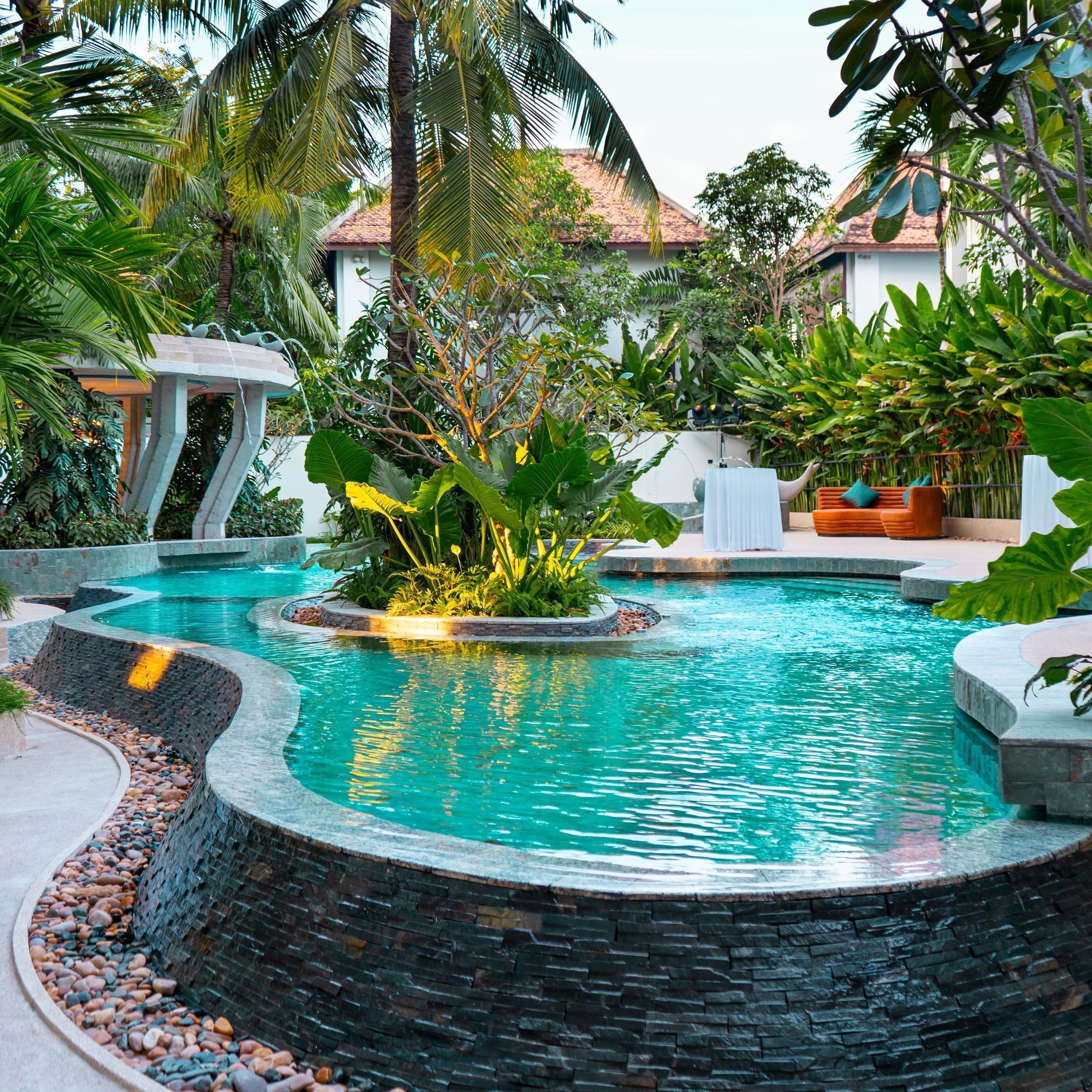 Une piscine bordée de pierres, entourée de plantes tropicales et de palmiers.
