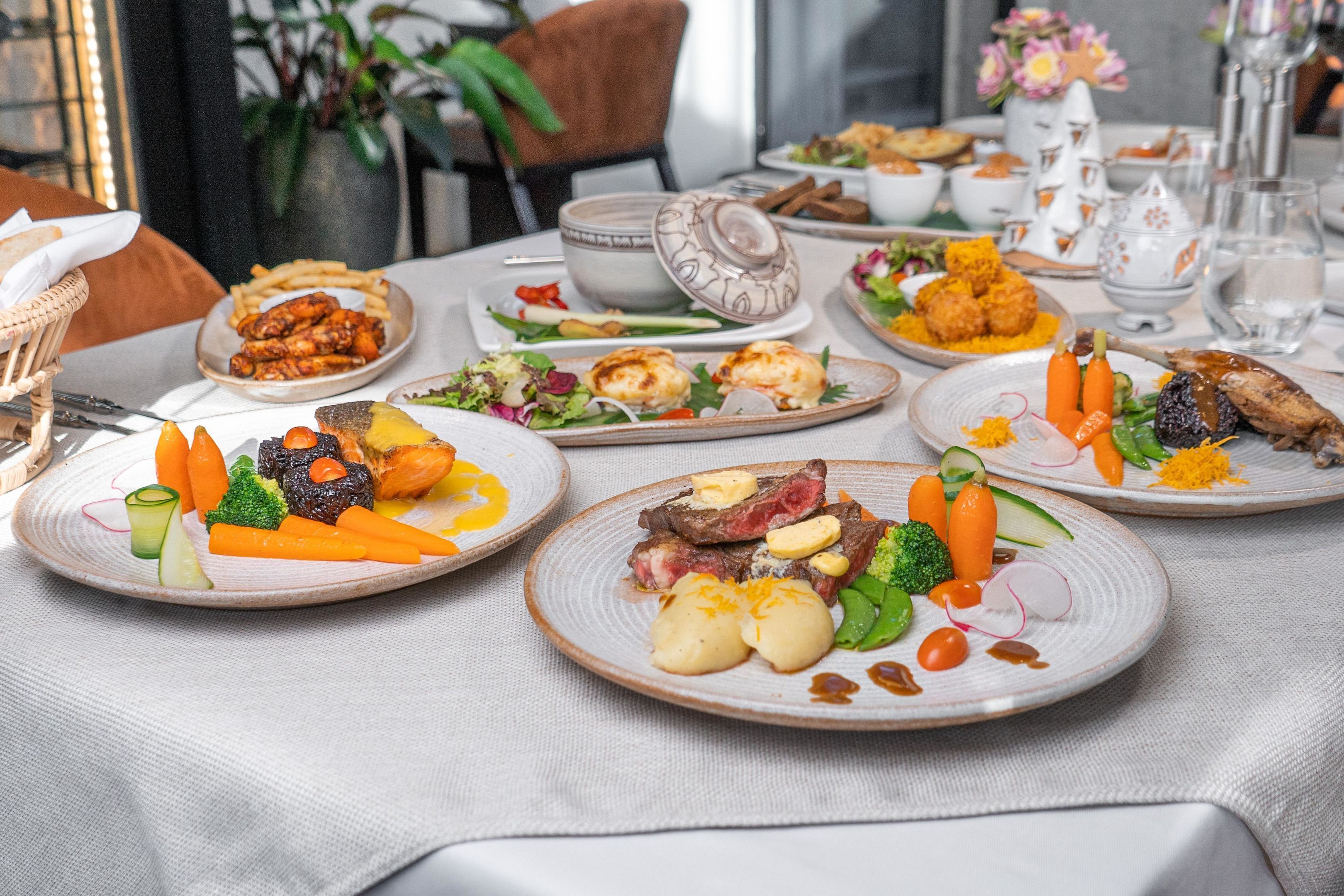 A dining table with various dishes, including steak, vegetables, and bread.