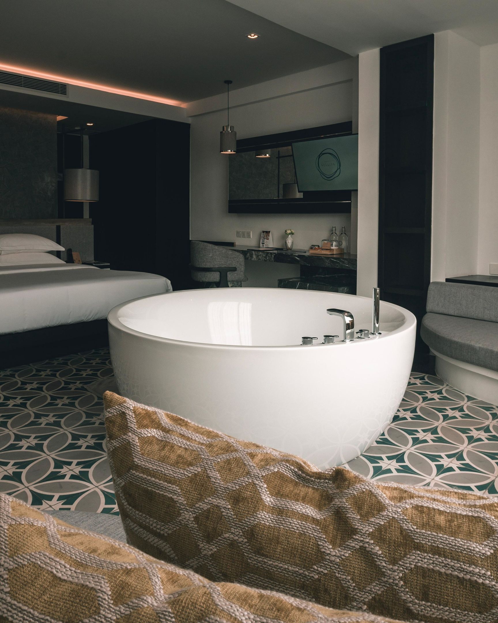 A modern bathroom with a freestanding bathtub, a large mirror, and a seating area with a patterned cushion.