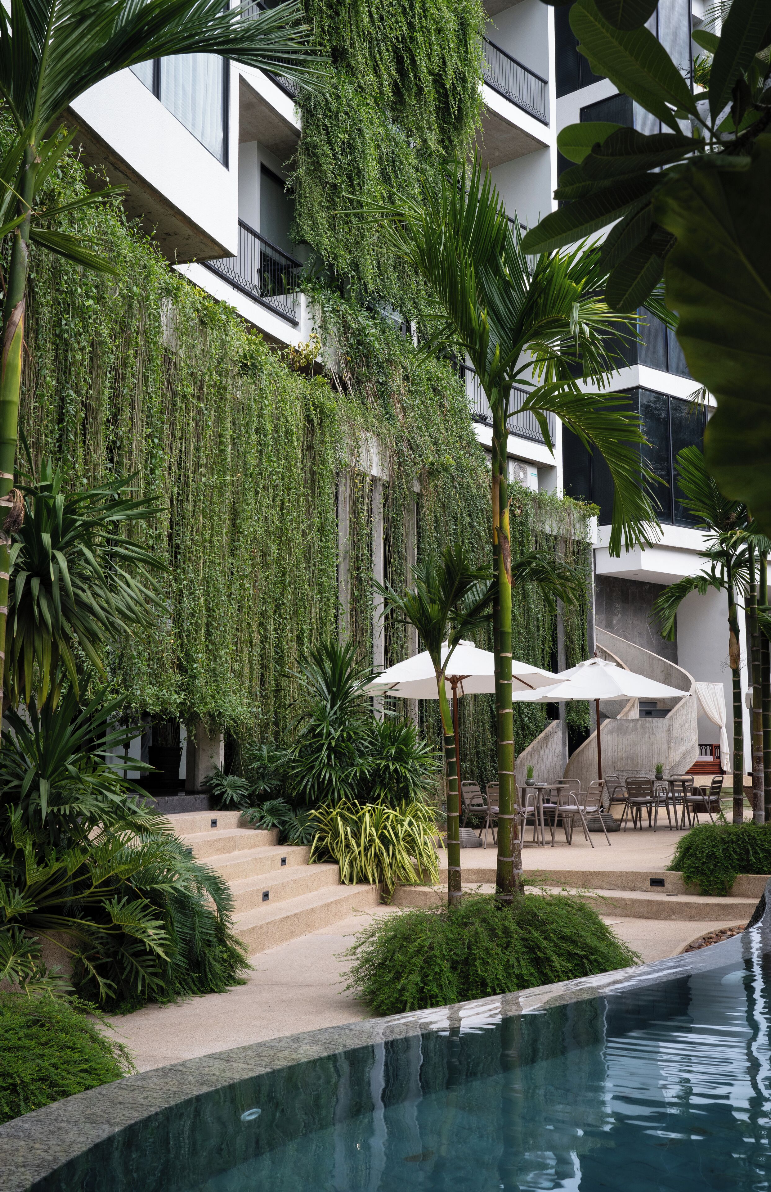 A modern building with a pool, surrounded by lush greenery and outdoor seating.