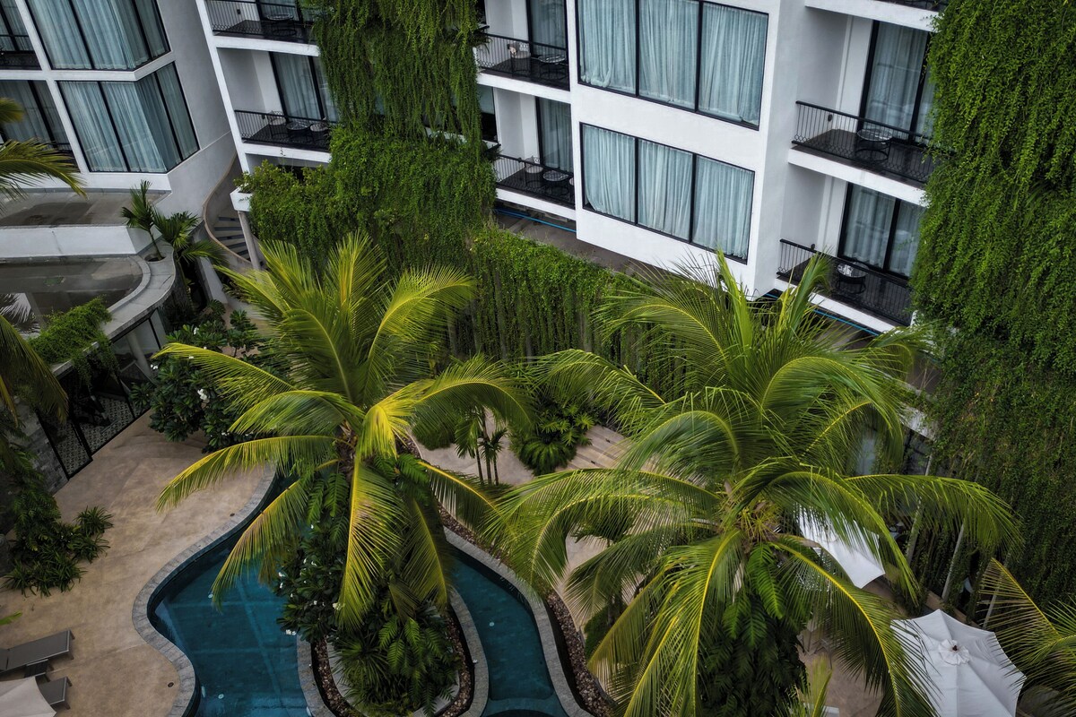 Un hotel moderno con piscina en la azotea, rodeado de palmeras y exuberante vegetación.