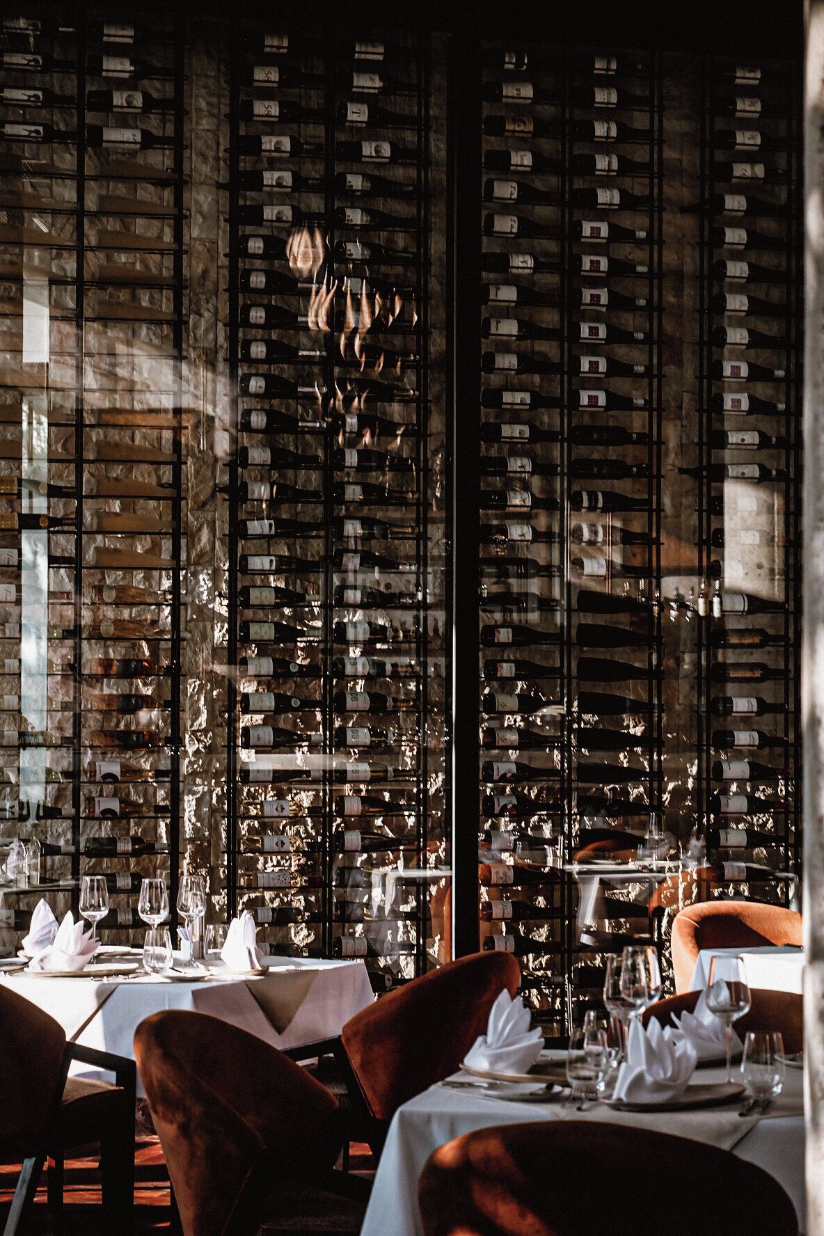 Interior de restaurante con mesas dispuestas para comer, una bodega en el fondo y una lámpara de araña.