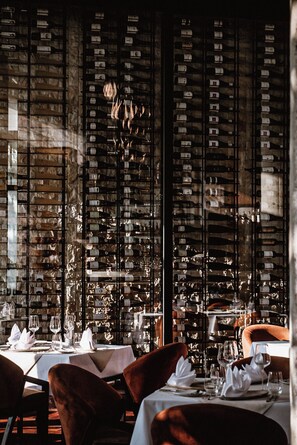 A restaurant interior with tables set for dining, a wine rack in the background, and a chandelier.