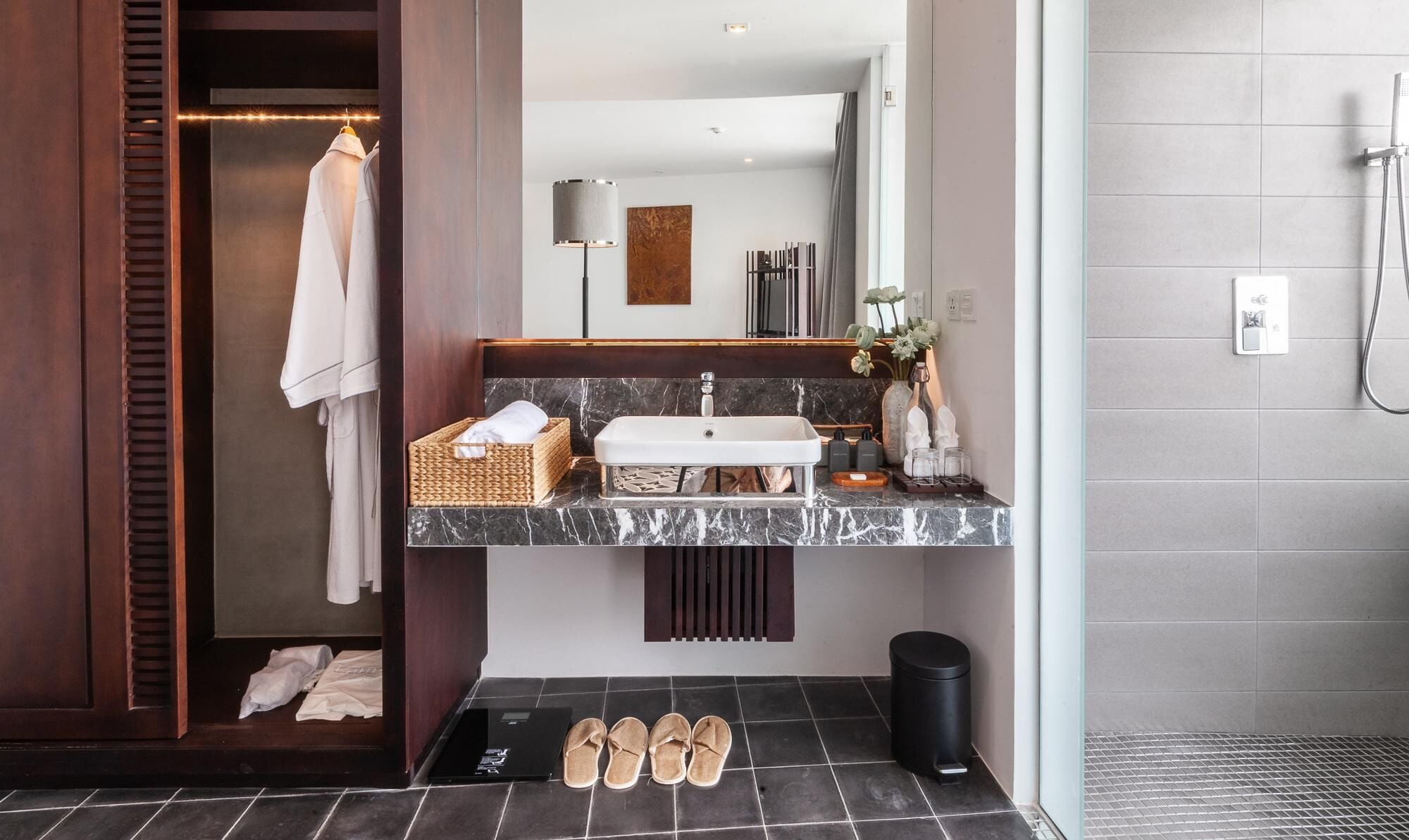 A modern bathroom with a marble sink, a mirror, a towel rack, a waste bin, and a shower area.