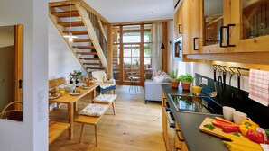 A modern kitchen with wooden cabinetry, a dining area with a wooden table and chairs, and a staircase leading to an upper level. - Vacation apartment Zur Tenne, 63 sqm upper floor, 2 separate bedrooms (Höslwang)