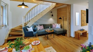 Ein gemütliches Wohnzimmer mit einer Holztreppe, einer Couch, einem gedeckten Esstisch und Holzboden.