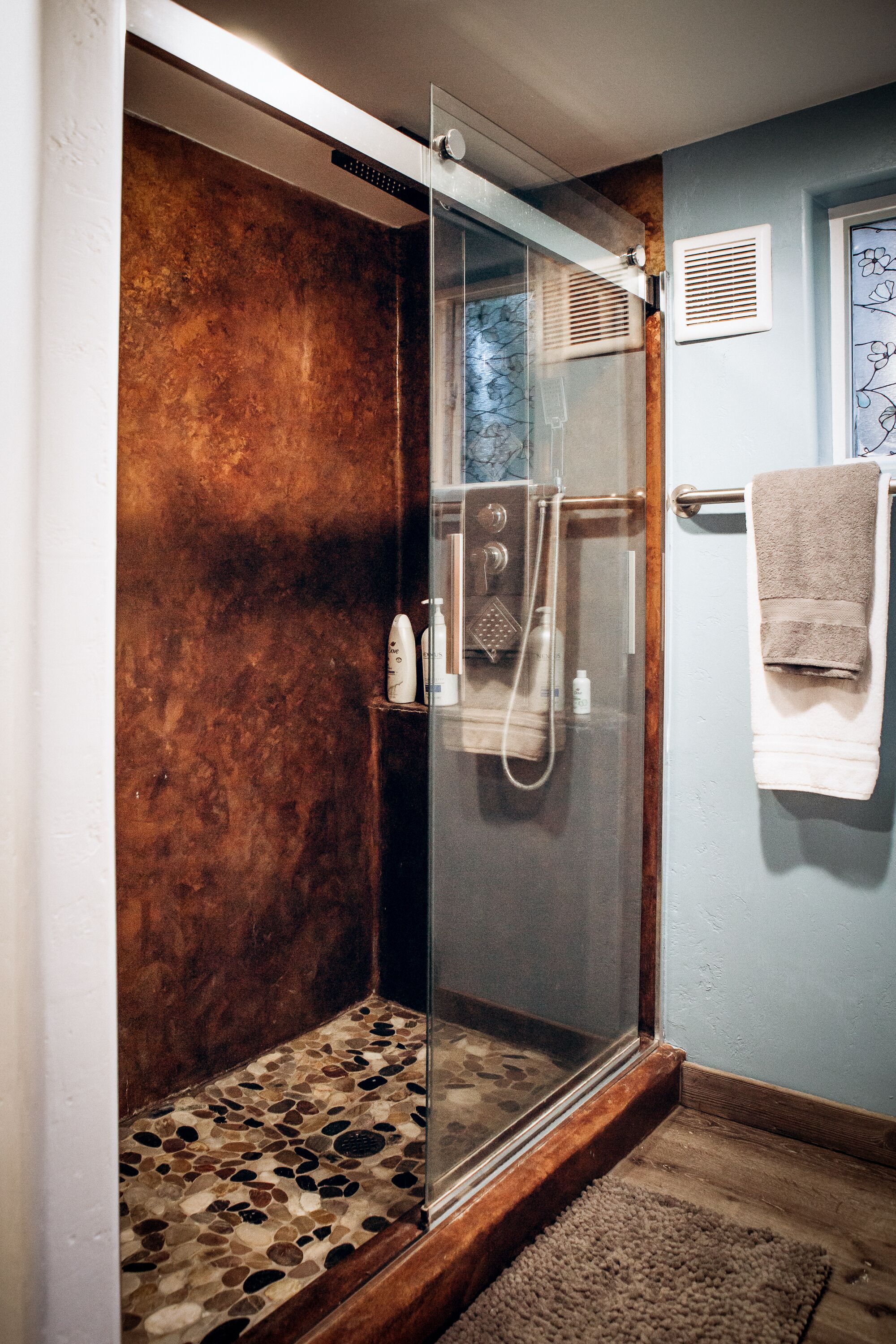 Eine gläserne Dusche mit strukturierter Wand, einem Handtuchhalter und einem kleinen Teppich.
