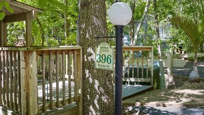 Un pontile in legno con un cartello che indica '396 Duene Dr' in una zona boschiva, con un lampione e una piccola costruzione.