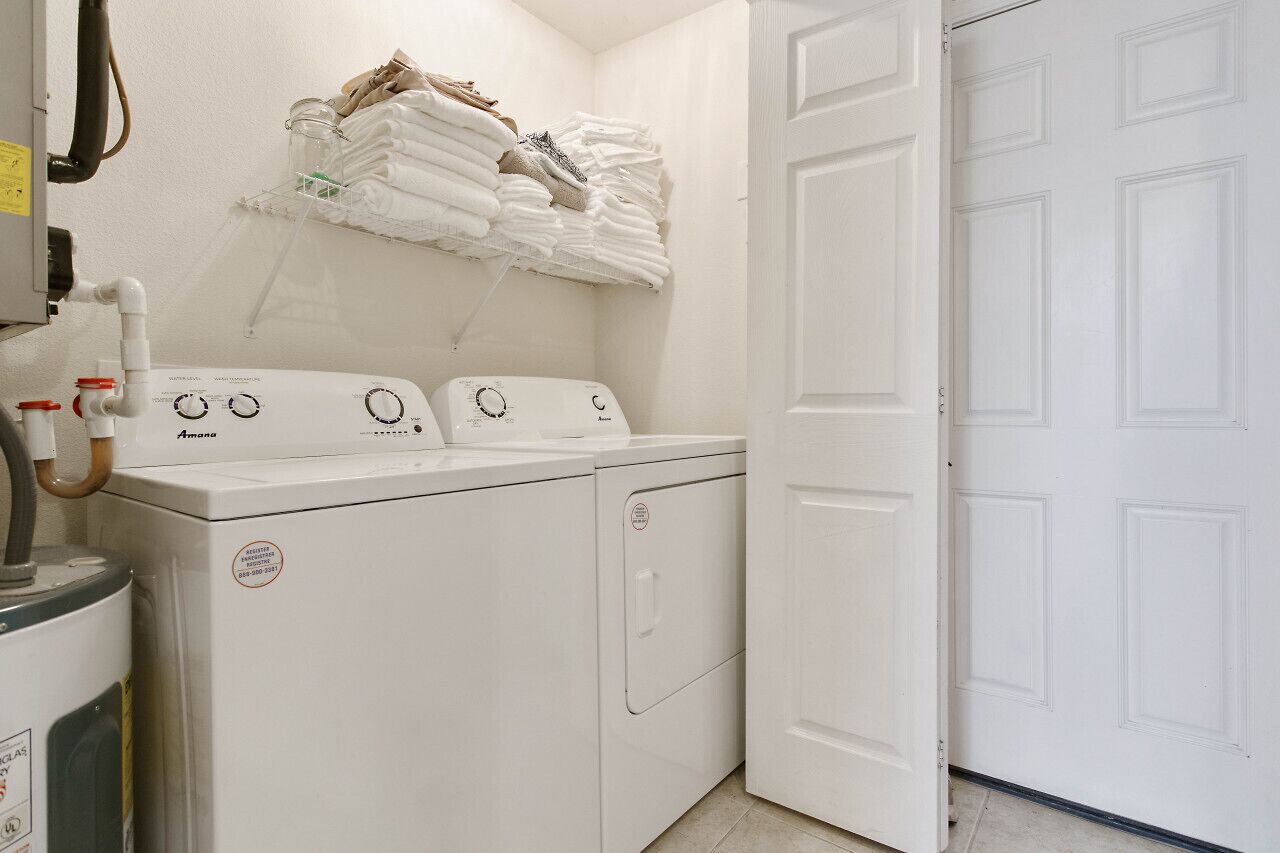 Een wasserette met een voorlader wasmachine en droger, een droogrek met opgevouwen handdoeken, en een gesloten deur.