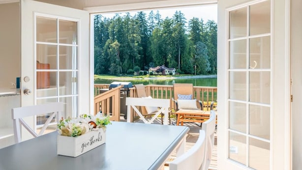 A balcony with a table and chairs, a grill, and a view of a lake and forest.