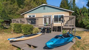 A cabin with a deck, two kayaks, and a paddleboard.