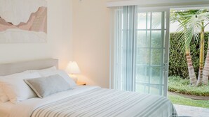 Une chambre à coucher avec un lit, une table de chevet, une lampe, une fenêtre et une vue sur un jardin.