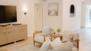 Un salon équipé d’un téléviseur à écran plat, de meubles en osier, d’un tableau et d’une porte donnant sur une autre pièce.
