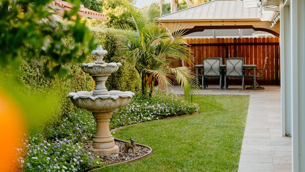 Un jardin bien entretenu, agrémenté d’une fontaine, d’un espace patio avec des chaises et d’un coin salon abrité.