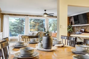 A dining area with a wooden table set for a meal, a ceiling fan, and a television mounted on the wall.