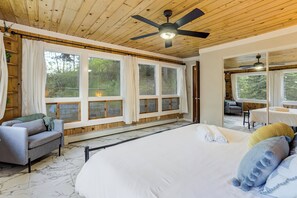 A bedroom with a large bed, a ceiling fan, and a view of the outdoors.
