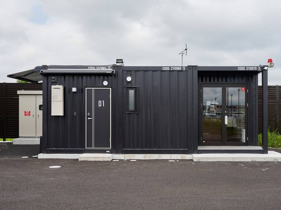 A modern, black building with two doors, each marked with a number. It features a small window and a security camera.