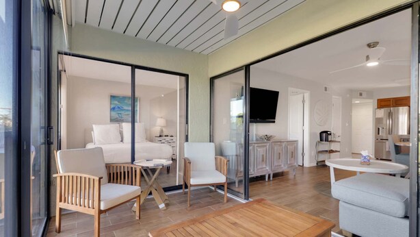 A hotel room with a bed, two chairs, a small table, a TV, a kitchen area, and a sliding glass door. - Cozy 1-bedroom condo with pool access (Marco Island)