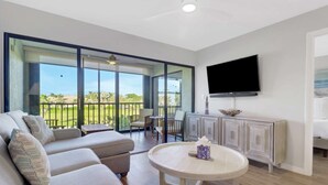 A modern living room with a sofa, a round table, and a TV mounted on the wall. - Cozy 1-bedroom condo with pool access (Marco Island)