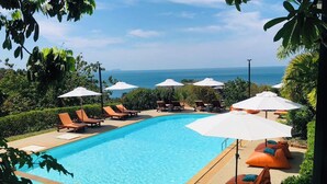 A swimming pool with lounge chairs and umbrellas, surrounded by greenery and overlooking a body of water. - Bakantiang Resort (Ko Lanta)