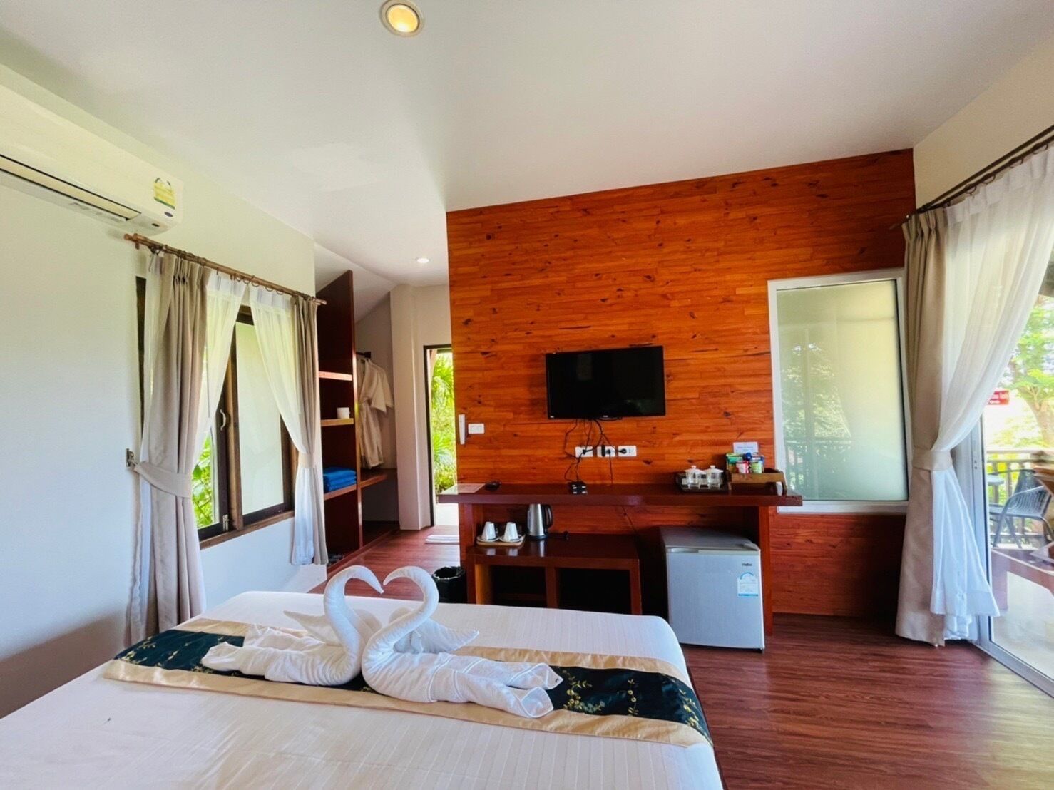 Una habitación de hotel con una cama, pared de madera, televisor, escritorio y ventana.