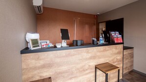 A reception desk with a coffee machine, a digital clock, a computer, and a small table. - HOTEL R9 The Yard Uki (Uki)